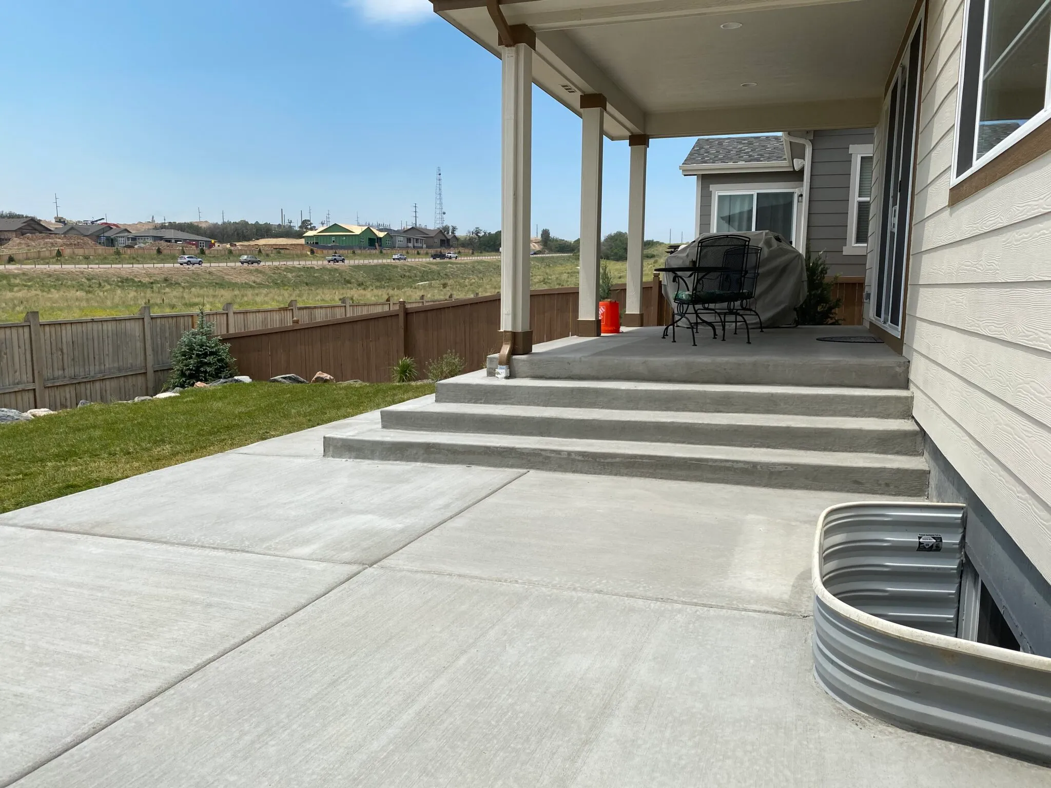 Broom-finish concrete patio with wide steps below a covered porch on an exposed residential lot
