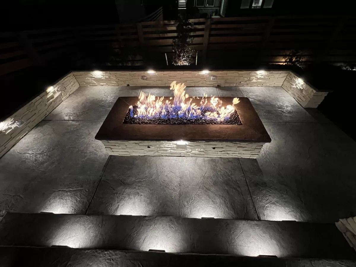 Rectangular built-in fire pit in a concrete patio with illuminated stone seating walls