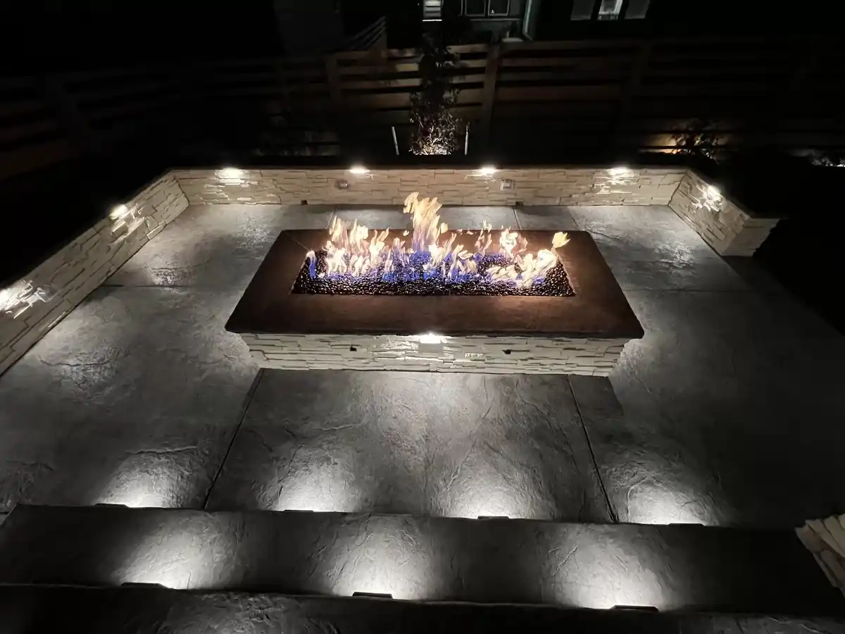 Rectangular built-in fire pit in a concrete patio with illuminated stone seating walls