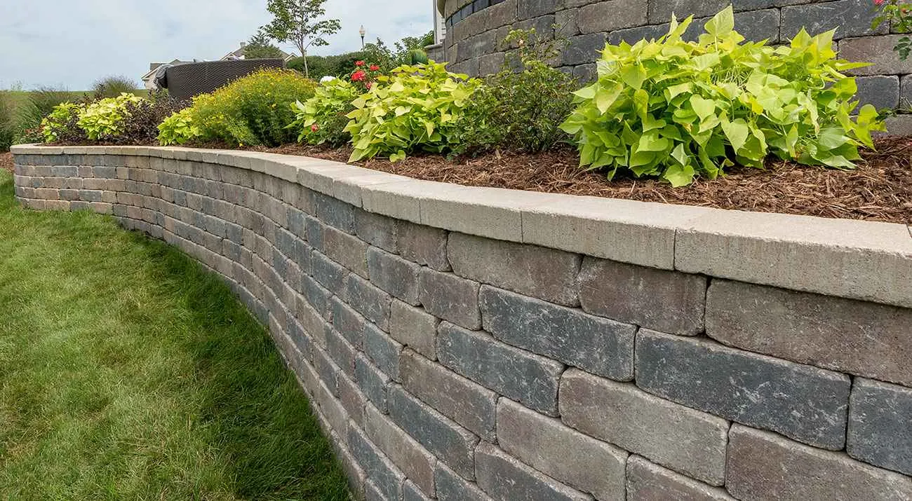 Curved segmental block retaining wall supporting a planted bed beside a lawn