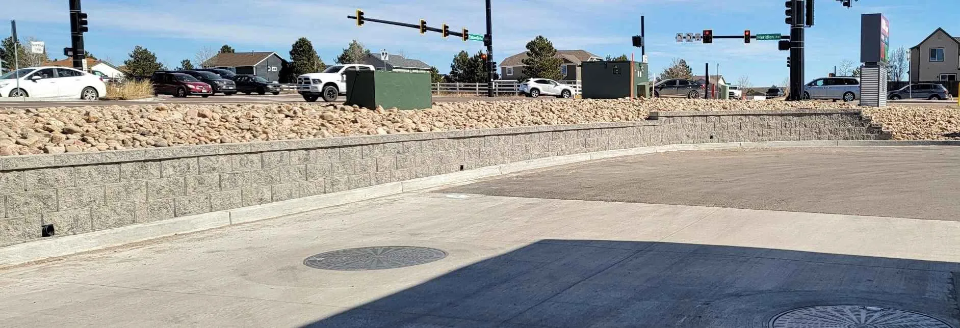 Long concrete block retaining wall beside a paved access area and rock-covered slope