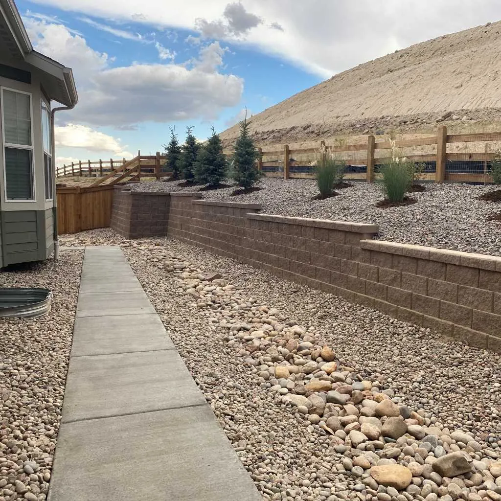 Block retaining wall beside a concrete walk and a visible rock drainage channel