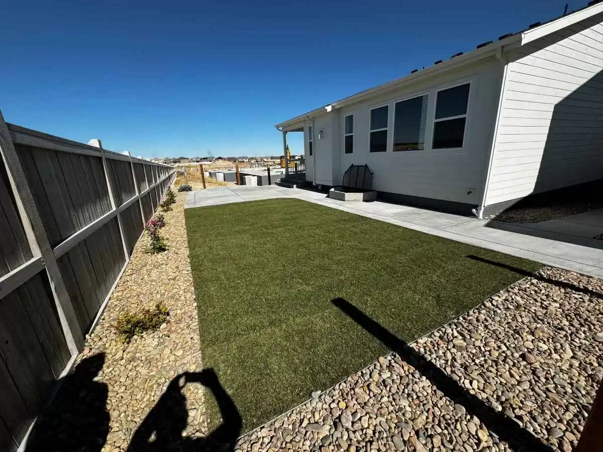 Finished green lawn bordered by decorative rock, small plants, and a concrete patio