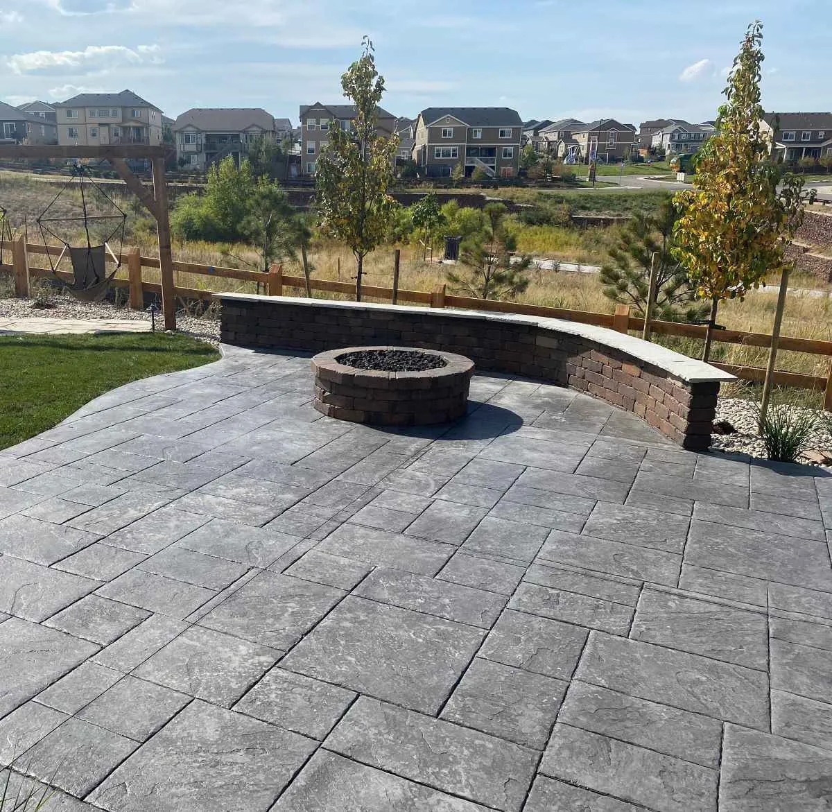 Stamped concrete patio with a fire-pit surround and curved seating wall, bordered by lawn and planted beds