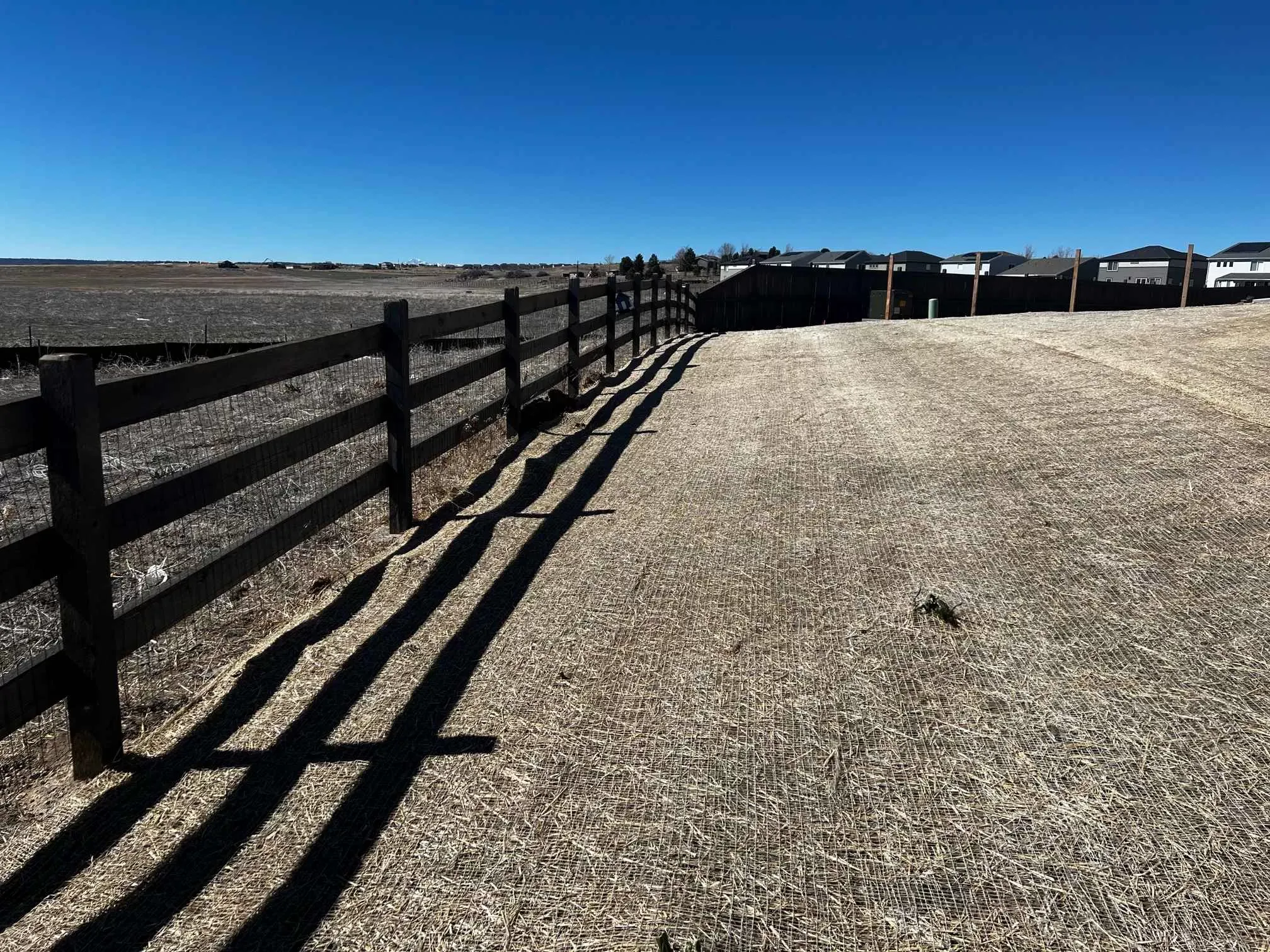 Wood rail fence with wire mesh beside a graded residential lot and open space