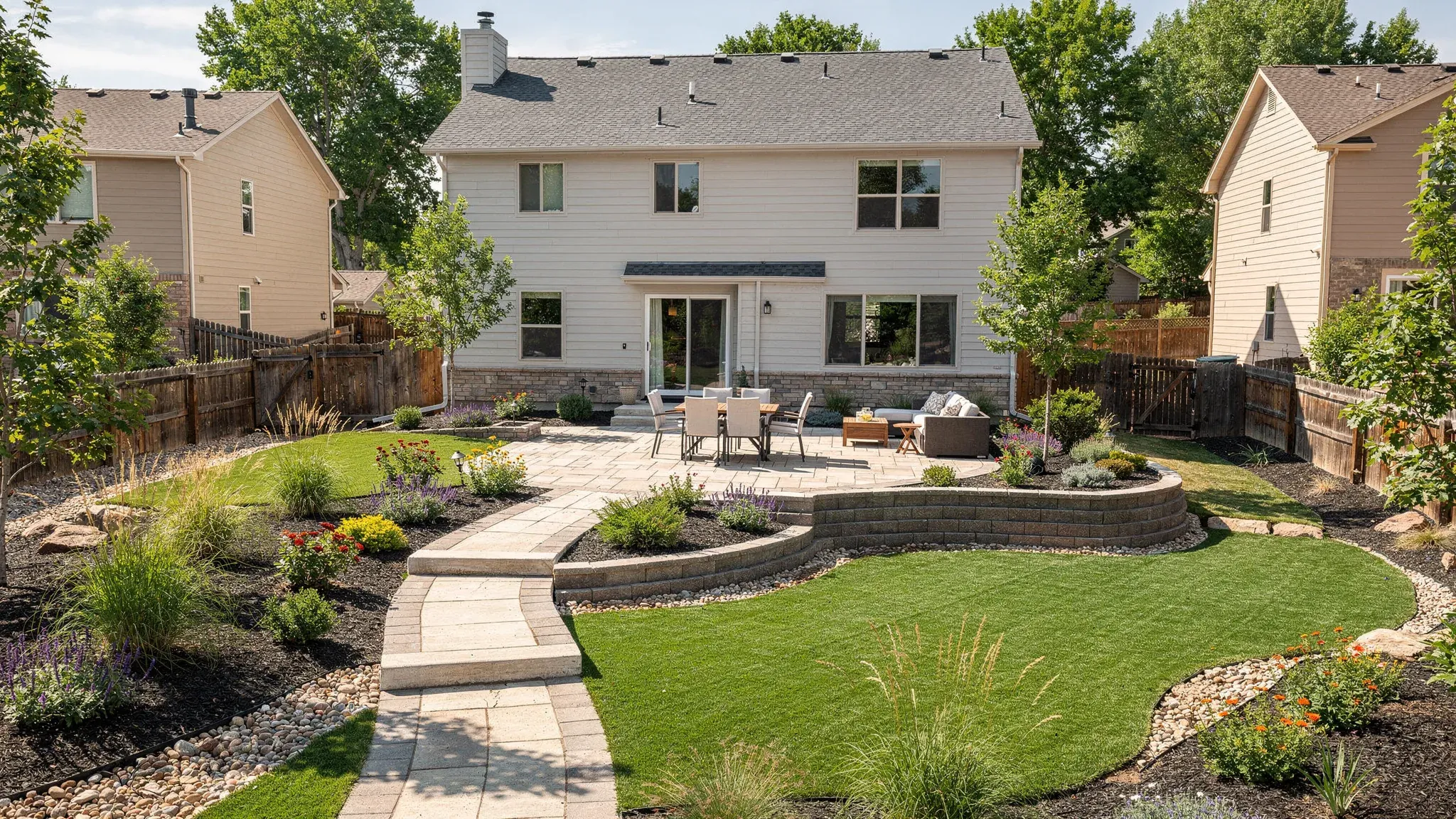 Custom residential landscape concept with a paver patio, connected walkway, curved lawn, layered planting, and low retaining walls