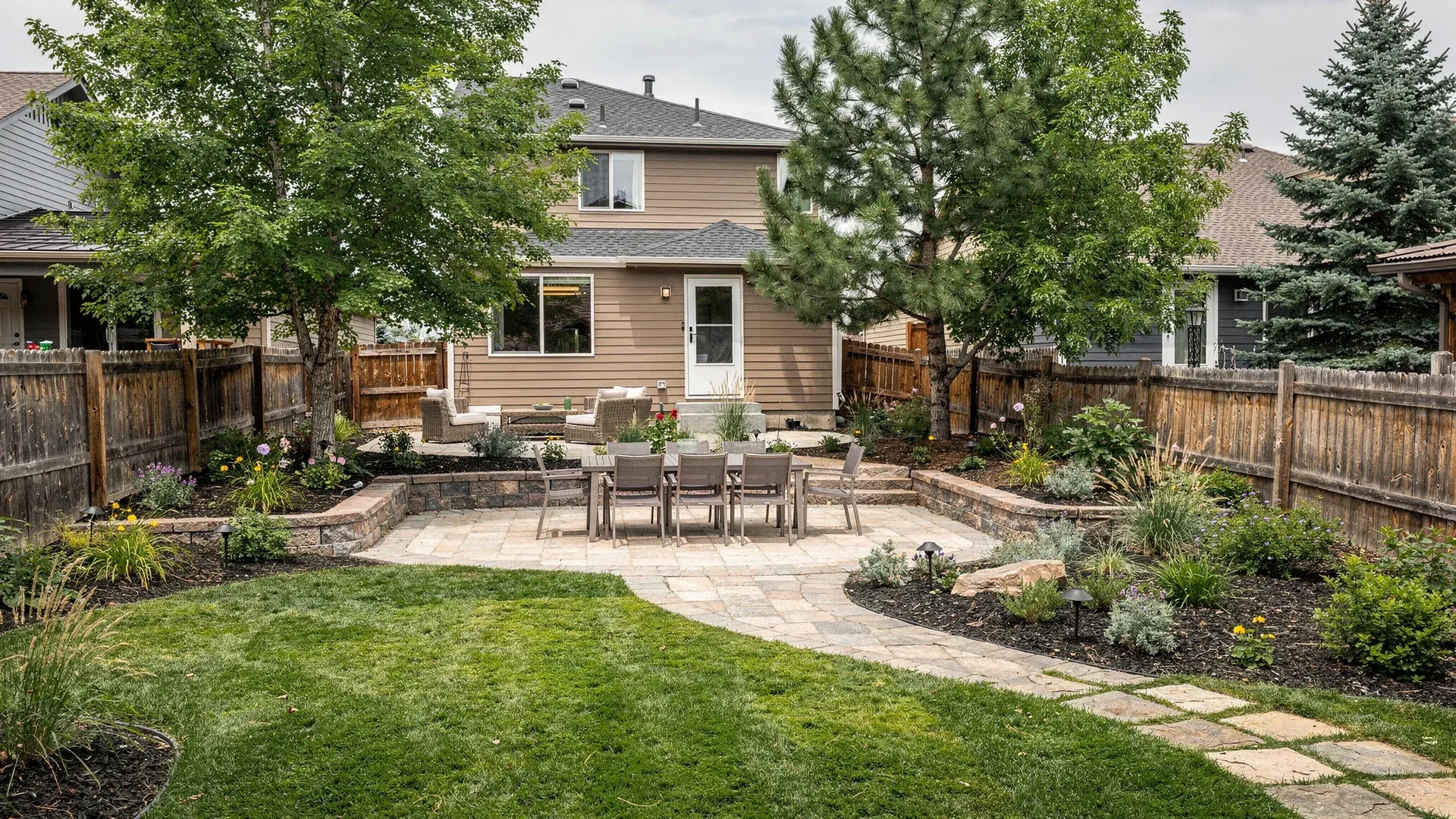 Residential landscape renovation concept for an established Highlands Ranch-style yard with mature trees, paver patios, connected walkways, lawn, low walls, and layered planting beds