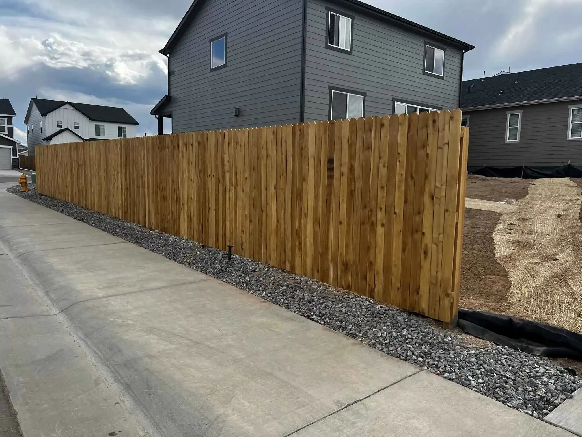 New wood privacy fence beside a concrete walk and an unfinished residential yard