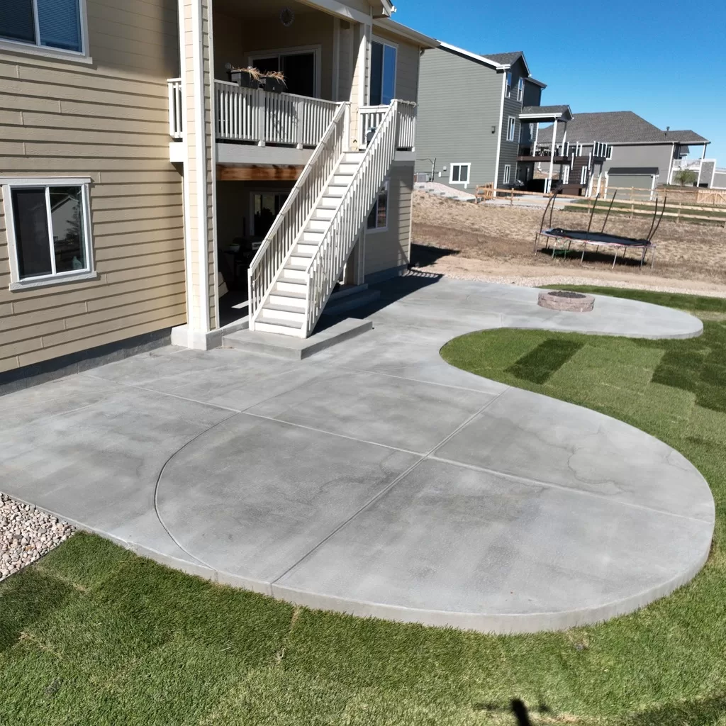 Spacious concrete patio with artistic curves blending into a lush lawn in a Castle Pines residence.