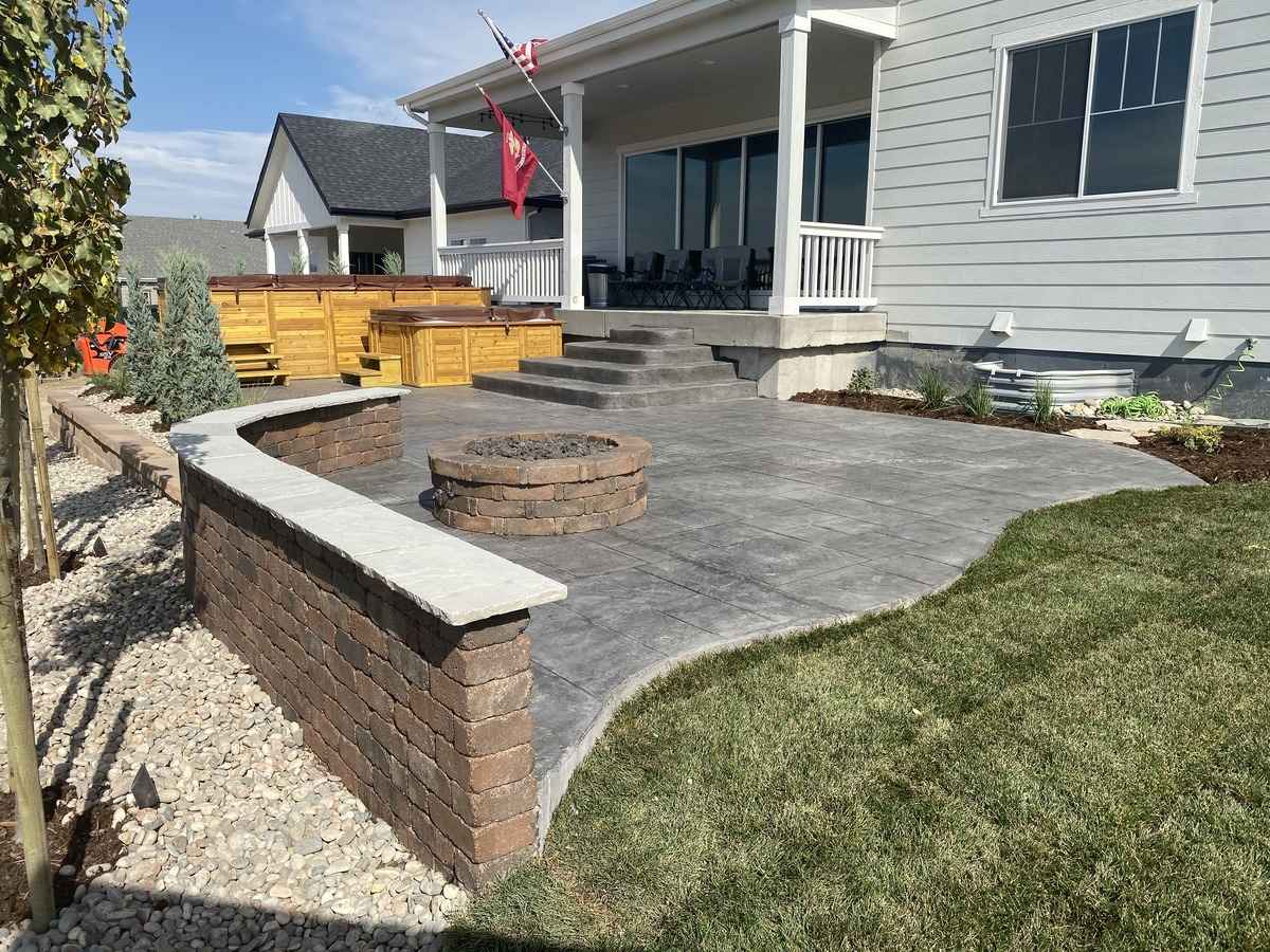 A well-appointed backyard with a stamped concrete patio, seating wall, fire pit, and fresh landscaping.