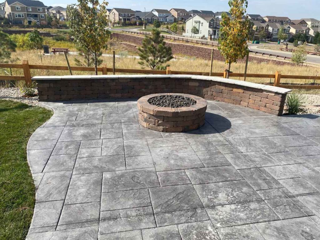 A beautifully designed backyard patio featuring a stamped concrete surface and a built-in fire pit with a stone wall in Parker, CO.