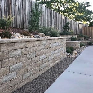 A professionally built Unilock Old Quarry block retaining wall with xeriscape landscaping, decorative rock, and a smooth concrete walkway.