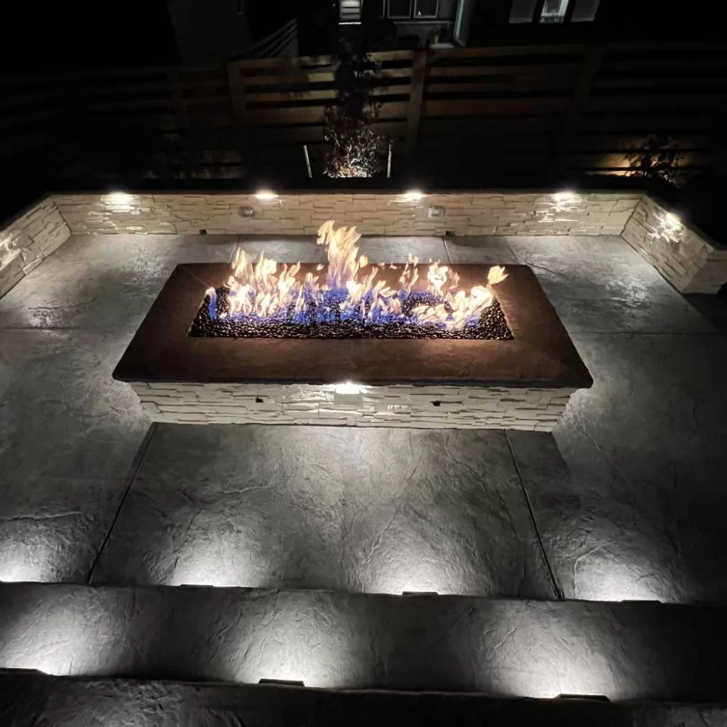 Rectangular gas fire pit with stone seating area and modern stamped concrete patio